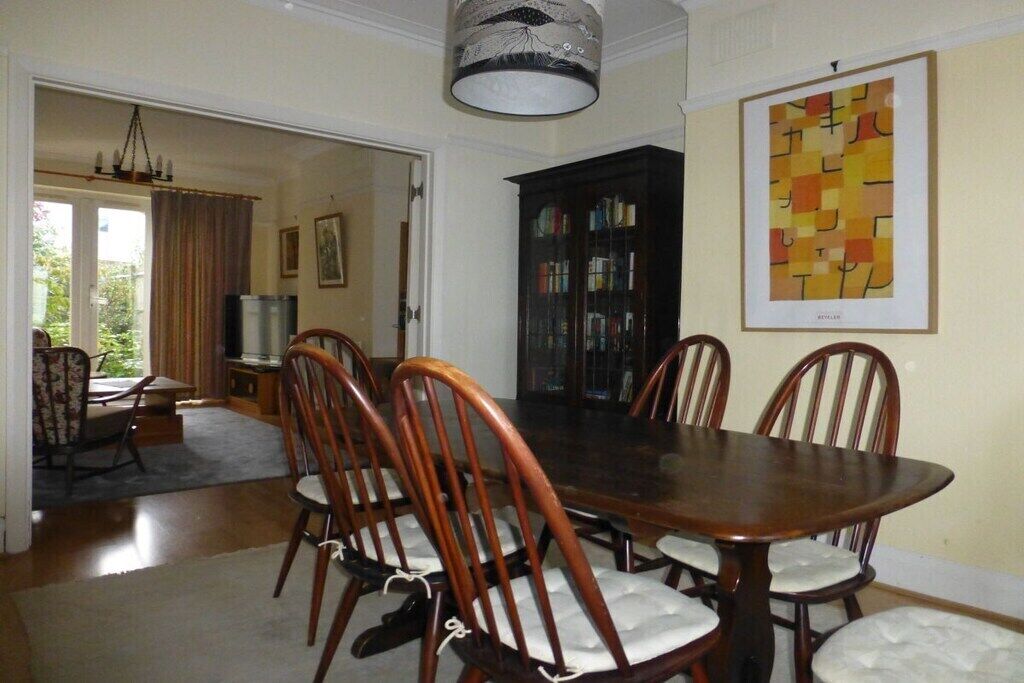 A dining room with a wooden table and chairs, a bookcase, and a chandelier.
