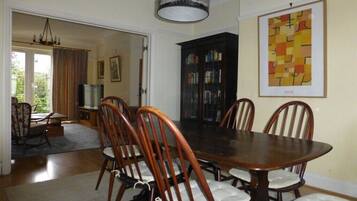 A dining room with a wooden table and chairs, a bookcase, and a chandelier.