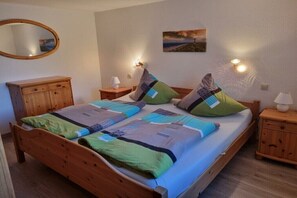 A bed with a wooden frame, a bedside table with a lamp, a wall-mounted mirror, and a painting on the wall. - Störtebeker holiday farm (Leybuchtpolder)