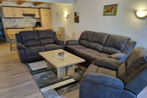 A living room with two grey sofas, a wooden coffee table, and a kitchen in the background. - Störtebeker holiday farm (Leybuchtpolder)