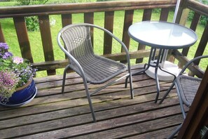 Eine Holzterrasse mit zwei Korbstühlen und einem kleinen runden Tisch.