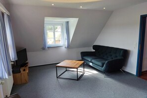 A modern living room with a sofa, a wooden coffee table, a television, and a window with curtains. - Hüs Lennies DG South (Nebel \/ Amrum)