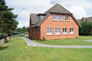 A two-story brick house with a sloped roof, a paved driveway, and a well-maintained lawn. - Hüs Lennies DG South (Nebel \/ Amrum)