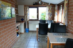 A compact kitchen with a dining area, featuring a window with curtains, a radiator, and a blue trash bin. - Holiday home with 3 bedrooms (Warmenhuizen)