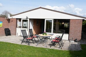 A patio with a table and chairs, a brick wall, and a sliding glass door. - Holiday home with 3 bedrooms (Warmenhuizen)