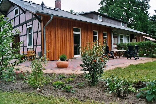 Ein traditionelles Haus mit Holzfassade, einem Ziegelweg und einem Gartenbereich mit Blumentöpfen und Gartenmöbeln.