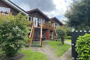 Eine Holzhütte mit einer Holztreppe, die zu einer Terrasse führt, umgeben von viel Grün.