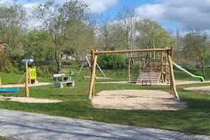 Ein Spielplatz mit Schaukeln, einer Rutsche und einer Kletteranlage.