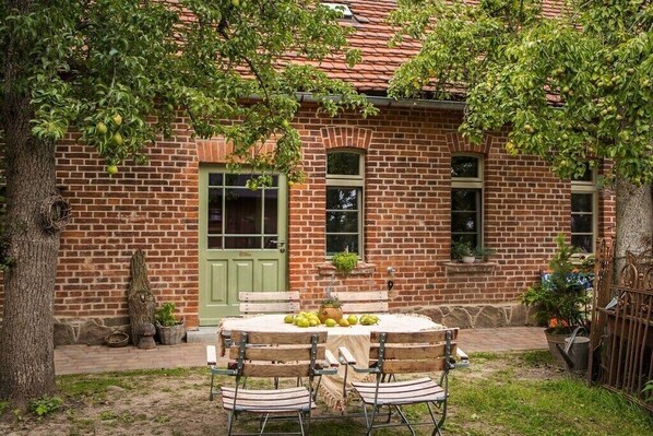 A brick building with a green door, a round table with chairs, and potted plants.