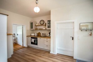 A compact kitchen with white cabinetry, a wooden countertop, a built-in oven, and a clock on the wall.