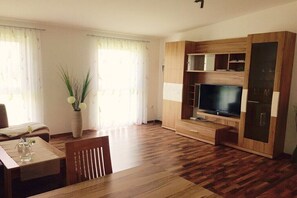 A living room with a wooden floor, a dining table, a TV on a wooden stand, and a vase with plants. - Holiday apartment with 1 bedroom (Attersee)