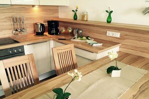 A modern kitchen with wooden countertops, a coffee maker, a kettle, and a small dining area with a chair and a table. - Holiday apartment with 1 bedroom (Attersee)