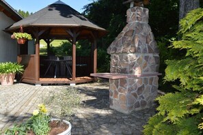 Ein Pavillon mit Steinofen, umgeben von Topfpflanzen und einer Pflasterterrasse.