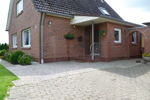 Ein zweistöckiges Backsteinhaus mit Ziegeldach, einer Veranda und einem kleinen Garten.