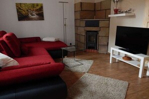 Un salon avec un canapé rouge, un téléviseur à écran plat, une cheminée et un tableau accroché au mur.