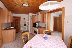 A compact kitchen with wooden cabinets, a dining table with a checkered tablecloth, and a ceiling fan.