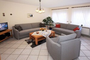 A living room with a grey sofa, a wooden coffee table, a TV, and a plant.