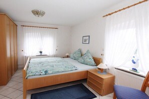 A bedroom with a bed, bedside table, chair, and window with curtains.