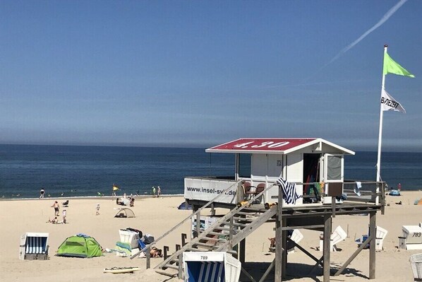 A lifeguard tower with a website sign, a green flag, and beach chairs. - Holiday apartment with 2 bedrooms (Westerland)