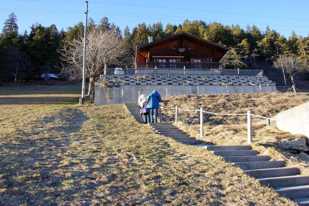 Eine Holzblockhütte mit Veranda, Außentreppe und einem umzäunten Bereich.