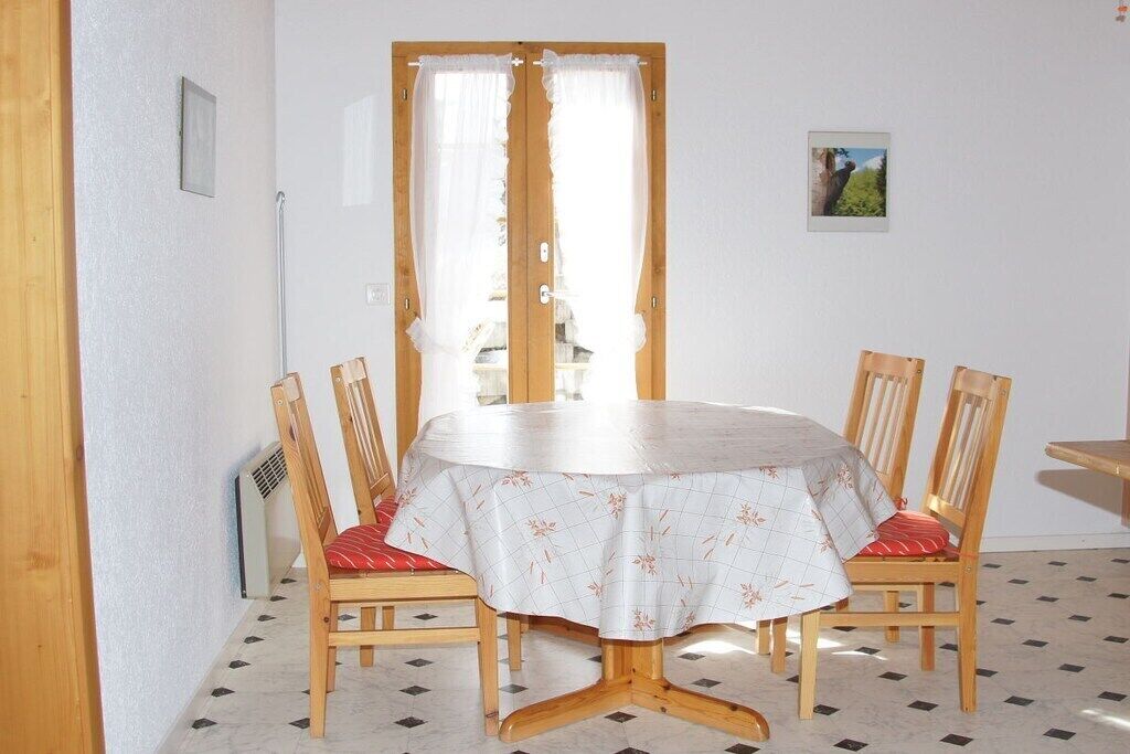 Ein Essbereich mit einem runden Tisch, vier Holzkästen, einer weißen Tischdecke und einer Tür mit Vorhängen.