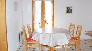 Ein Essbereich mit einem runden Tisch, vier Holzkästen, einer weißen Tischdecke und einer Tür mit Vorhängen.