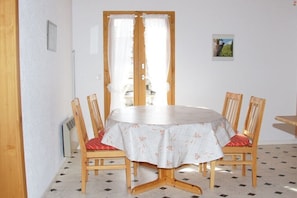 Ein Essbereich mit einem runden Tisch, vier Holzkästen, einer weißen Tischdecke und einer Tür mit Vorhängen.