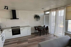 A compact kitchen with a gas stove, oven, and white cabinets. There's a dining area with a table and chairs, and a sofa in the foreground. - 1A5 Family Moritz Koopman (Petten)