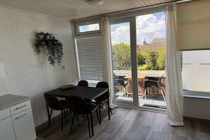 A dining area with a table and chairs, a window with blinds, and a view of the outdoors. - 1A5 Family Moritz Koopman (Petten)