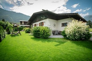 Ein traditionelles Chalet mit einem geneigten Dach, einem gepflegten Garten und einem Berg im Hintergrund.