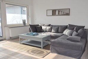 Ein Wohnzimmer mit einem grauen Sofa, einem Glastisch und einem gerahmten Bild an der Wand.