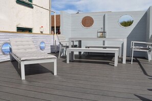 Eine Dachterrasse mit einer weißen Liege, einem weißen Tisch und einer weißen Bank.