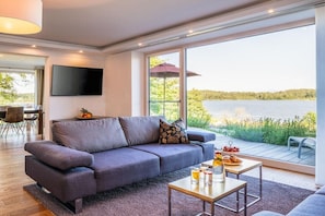 Ein modernes Wohnzimmer mit einem grauen Sofa, einem Flachbildfernseher und einem Essbereich mit Tisch und Stühlen.