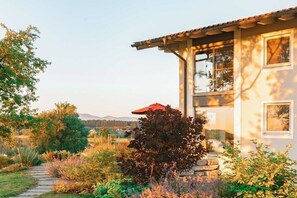 Ein Haus mit einem gepflasterten Weg zum Eingang, umgeben von üppiger Vegetation und einer Aussicht auf Hügel in der Ferne.