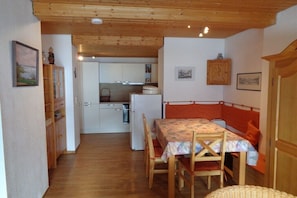A compact room with a dining table, chairs, a bed, a small kitchenette, and a wooden ceiling. - Holiday apartment with 2 bedrooms (Riezlern)