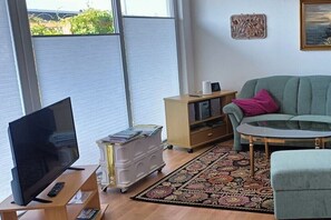 A living room with a TV on a stand, a sofa, a glass coffee table, a patterned rug, and a wooden cabinet. - Holiday home with 2 bedrooms (Fehmarn OT. Staberdorf)