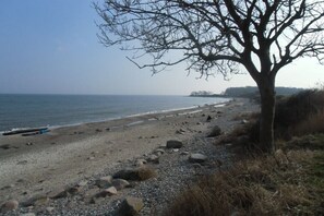 A beach with a tree, pebbles, and a calm sea. - Holiday home with 2 bedrooms (Fehmarn OT. Staberdorf)