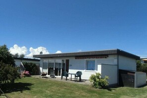 A single-story mobile home with a front porch, a small patio area, and a visible garage door. - Holiday home with 2 bedrooms (Fehmarn OT. Staberdorf)