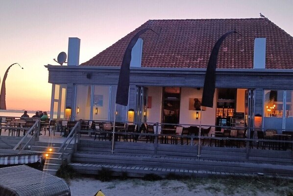 A seaside restaurant with outdoor seating, a terrace, and a view of the ocean. - Holiday home with 2 bedrooms (Fehmarn OT. Staberdorf)