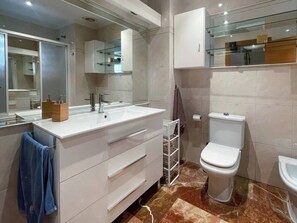 Un baño moderno con tocador blanco, un espejo grande, un inodoro y un estante de vidrio sobre el lavamanos.