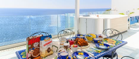 Een ontbijttafel met uitzicht op zee, een wit kastje en een glazen balustrade.
