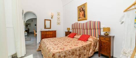 A bedroom with a bed, a nightstand, a lamp, a painting, and a wardrobe.