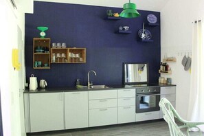 A modern kitchen with a dark blue backsplash, stainless steel appliances, and a green pendant light. - Holiday home with 1 bedroom (Schönwalde-Glien)