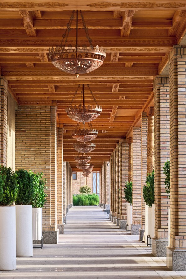 Un corredor cubierto con varios candelabros colgantes, paredes de ladrillo y plantas en macetas.
