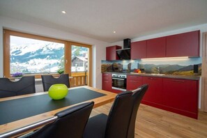 Eine moderne Küche mit roten Schränken, einem Holzespeisetisch und Blick auf Berge.