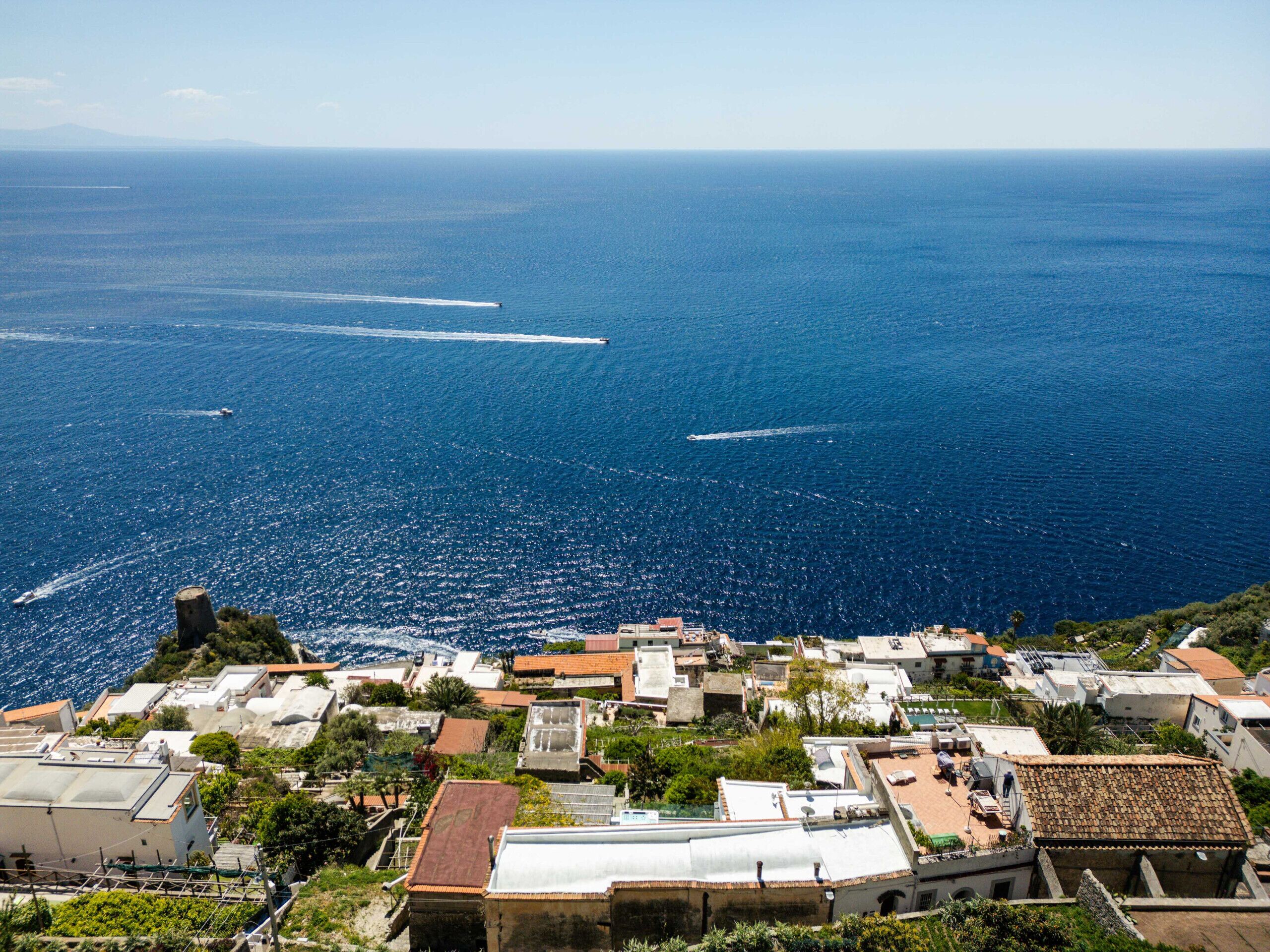 Une ville côtière avec des bâtiments, une vue dégagée sur la mer et une montagne qui se profile à l’horizon.