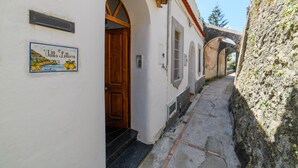 A narrow alleyway with a white building, a wooden door, and a sign with a coastal scene. - Estate4home - Villa Lettieri (Praiano)