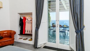 A room with a brown leather sofa, a clothing rack with various garments, and a view of an outdoor patio with a table and chairs. - Estate4home - Villa Lettieri (Praiano)