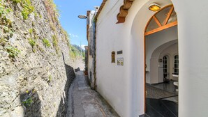 A narrow alleyway with a stone wall on one side and a building entrance with a tiled floor and a door. - Estate4home - Villa Lettieri (Praiano)
