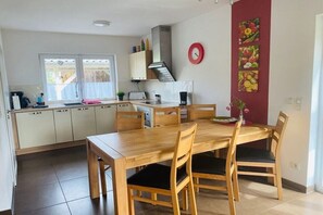 Eine moderne Küche mit Holzschränken, einem Esstisch mit Stühlen, einer roten Uhr und einer Wanddekoration mit Obstmotiven.